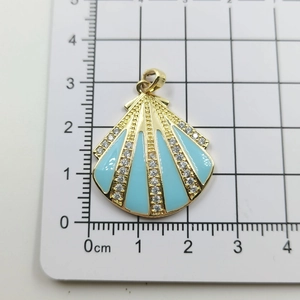 Detail eines blauen Muschel-Anhängers mit Goldbeschichtung und Kristallen auf Messraster