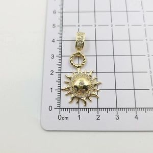 Detailed shot of golden sun pendant with zircon studs on a white measuring grid board