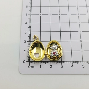 Detail view of gold egg locket with silver bear and red heart over measurement scale