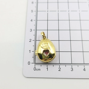 Detailed view of an oval locket pendant with More Self Love engraving and red heart stone