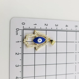 Detailansicht der goldenen Hamsa-Kette mit Zirkonia und blauem Auge auf einer Skala
