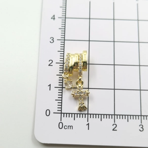 Detailed size measurement of a gold cross pendant with micro-inlaid stones on a ruler