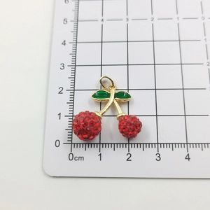 Macro shot of sparkling red rhinestone cherry pendant with green enamel leaf on a scale