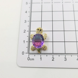 Macro detail of a 18k gold turtle pendant with zircon accents and a purple gemstone