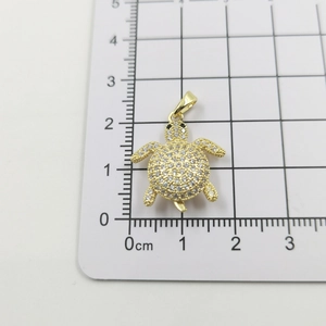 Macro detail of a 2cm 18k gold plated sea turtle pendant with micro-set zircon stones
