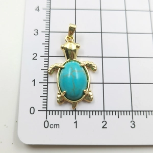 Macro scale shot showing a gold turtle pendant size about 3.5cm with turquoise stone