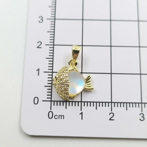 Macro shot of gold fish pendant with zircon inlay and moonstone on a measurement grid