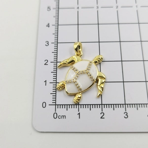 Macro shot showing dimensions of golden turtle pendant with white enamel and zircons