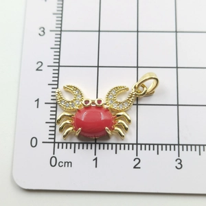 Macro view of gold crab pendant with red stone and zircons measuring 2cm wide