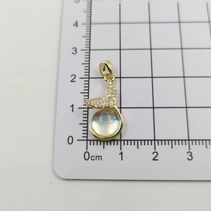 Macro shot of gold-plated mermaid tail pendant with iridescent stone and zircon inlay
