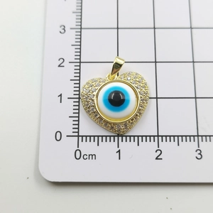 Macro detail of gold evil eye heart pendant on scale showing 2cm size measurement