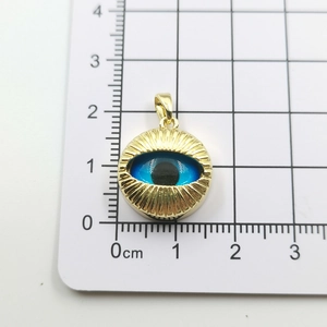 Detail view of gold-plated evil eye pendant on a metric grid showing the actual size