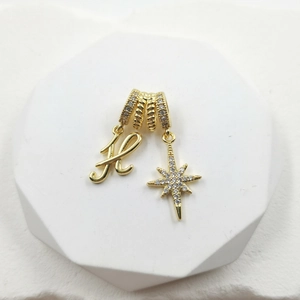 Detail of gold-plated charm featuring zircon-set letter H and North Star pendant design