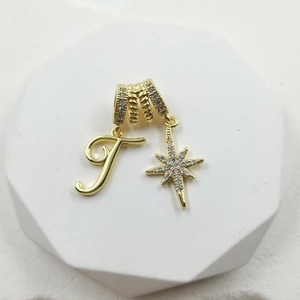 Close-up of gold pendant with textured ring, letter T and pavé zircon star detail
