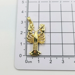 Detailed view of gold lobster pendant with zircon inlay on a centimeter scale board