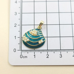 Macro shot of gold seashell pendant with green enamel and small white pearls on a ruler