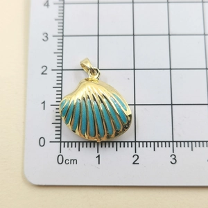 Detailed view of sea shell pendant in gold and turquoise enamel on measurement grid