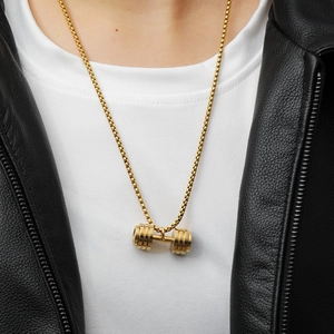 Detail of a polished gold dumbbell pendant necklace worn with a leather jacket