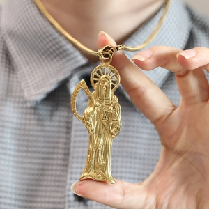 Gros plan détaillé du pendentif Santa Muerte doré avec relief et sa chaîne en métal