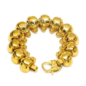 Dettaglio ravvicinato del bracciale dorato a teschi con occhi in pietra verde