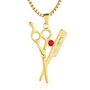 Makroaufnahme von Schere und Kamm Anhänger in Gold mit rotem Edelstein an Kugelkette
