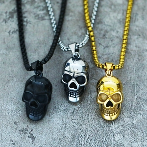 Detailed view of three skull pendants in black, silver and gold finishes on stone background