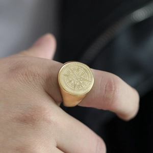 Primer plano de anillo de sello dorado con brújula y estrella grabada en acero mate