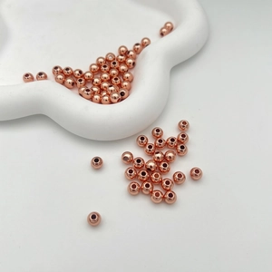 Perline rotonde in oro rosa lucido per gioielli fai-da-te su piatto decorativo bianco