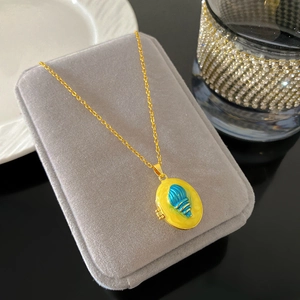 Detalle del collar de relicario ovalado en esmalte amarillo con diseño de concha azul marino