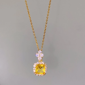 Macro view of gold chain necklace featuring a square yellow gem with halo diamonds