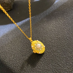 Macro detail of vintage gold locket necklace with yellow enamel and central pearl inlay