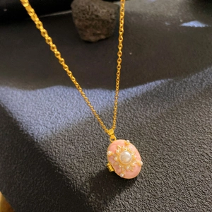 Detailed close-up of pink oval sunburst pendant with white pearl on gold chain