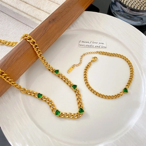 Parure de bijoux dorés avec cœurs en zircone verte et chaîne gourmette sur plateau blanc