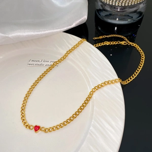Détail macro d'un collier à maille gourmette dorée avec pendentif coeur en zircon rouge