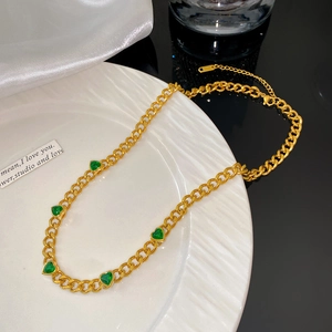 Gros plan du collier à grosse chaîne dorée avec cinq breloques cœurs en zircon vert