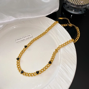 Gros plan du bracelet en chaîne dorée avec cinq pendentifs cœurs noirs sur un plat blanc
