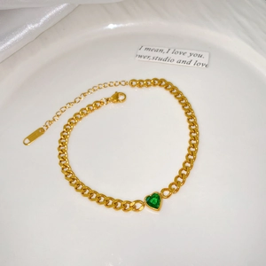 Détail d'un bracelet doré avec zircon vert en forme de cœur et fermoir mousqueton