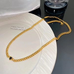 Détail d'un collier à mailles cubaines dorées avec pendentif cœur noir sur soie