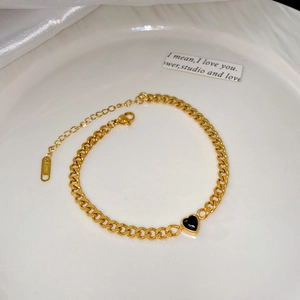 Détail de bracelet à chaîne gourmette dorée avec pendentif cœur noir et logo en acier