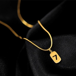 Detail view of a gold snake chain necklace with a polished rectangle number 7 pendant