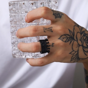Close-up of gothic black crown ring on tattooed finger holding a textured glass