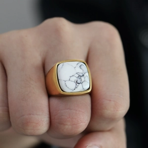 Gros plan d'une bague pour homme en acier titane doré avec une pierre howlite carrée