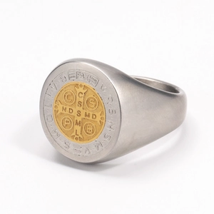 Makroaufnahme des St. Benedikt Siegelrings mit goldenem Kreuz und lateinischer Gravur