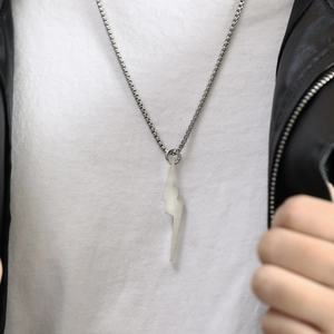 Close-up of a white lightning bolt pendant on a silver box chain worn with a leather jacket