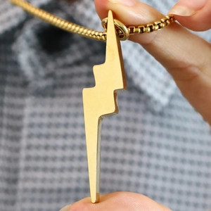 Macro detail of gold lightning bolt pendant on a square venetian chain held in hand