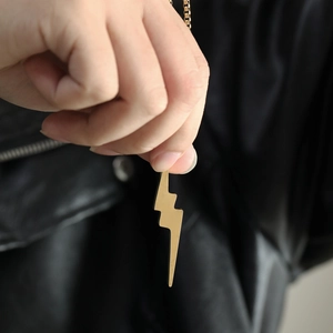 Close-up of hip hop golden lightning bolt pendant necklace held against black leather background