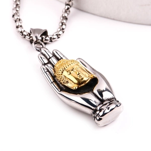 Macro shot of silver retro palm holding a golden Buddha head pendant on a box chain
