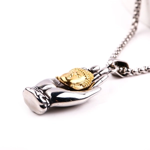 Macro shot of silver metal palm pendant holding a golden Buddha head with steel chain