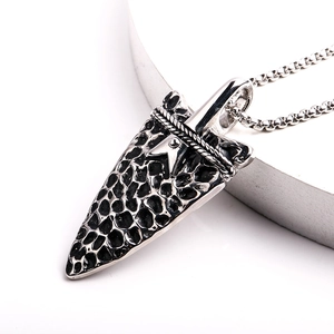Macro detail of industrial arrow pendant with rock texture and star inlay on box chain