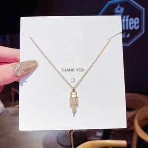 Detailed view of a gold lock and key necklace with crystal pavé on white gift card